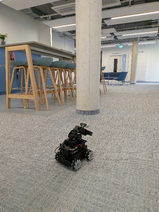 The robot, a four-wheeled base with an arm and a camera on the gripper